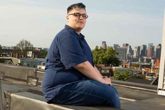 Participant Cameron sitting on a roof top with a view of the city in the background