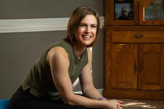 Participant Stephanie - person with short brown hair wearing a green tank top smiling in front of a grey wall