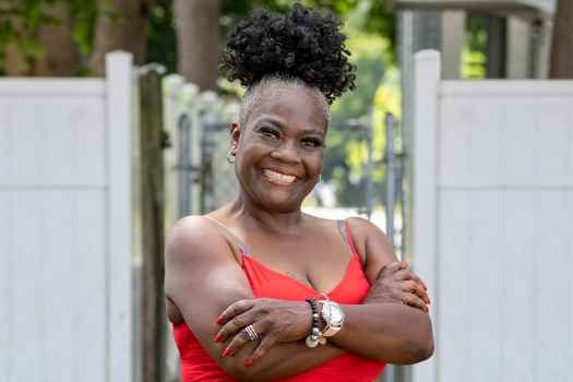 Participant Norma - person with dark curly hair wearing a red dress smiling outside
