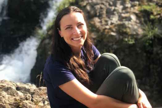 Participant Natalia - person with long brown hair sitting on a large rock outside