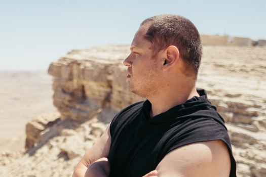 Deconstructing Stigma participant Lavih - Person stands outside in desert with boulder behind