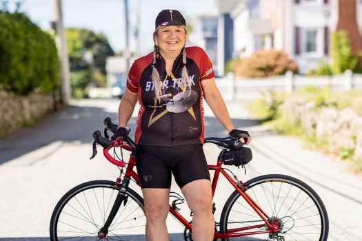 Participant Pata - person with long grey hair smiling outside in front of a bicycle