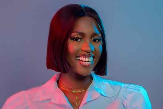 Participant Mailiana - person with short brown hair wearing a white shirt smiles in blue and red lighting