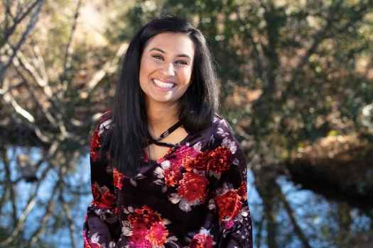 Participant Vaidehi - person with long dark hair wearing a red and black floral patterned shirt smiling outside