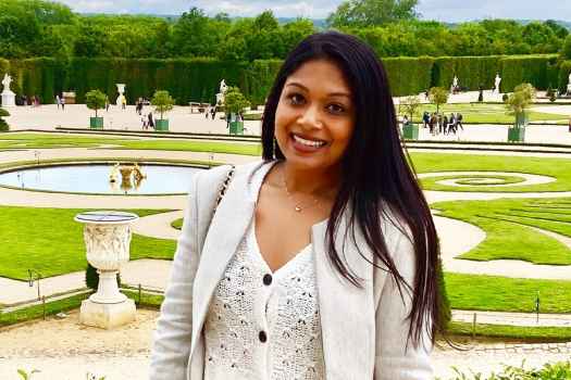 Participant Subrina - person with long dark hair smiling in front of a garden