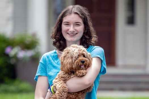 Participant Caroline - person with short brown hair holding a dog and smiling outside
