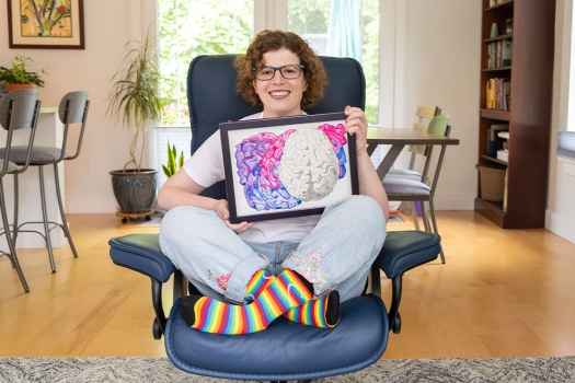 Participant Caitlin - person with short curly hair and glasses smiling, holding a framed illustration