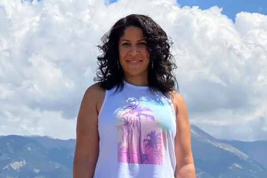 Participant Bianca - person with long dark hair smiling in front of a blue sky with puffy clouds