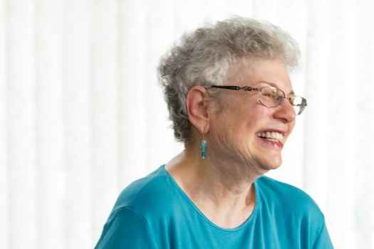 Participant Carol - person with short white hair wearing teal and smiling in front of a bright white background