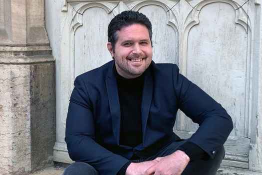 Participant Christophe - person with short dark hair smiling outside in front of a stone structure