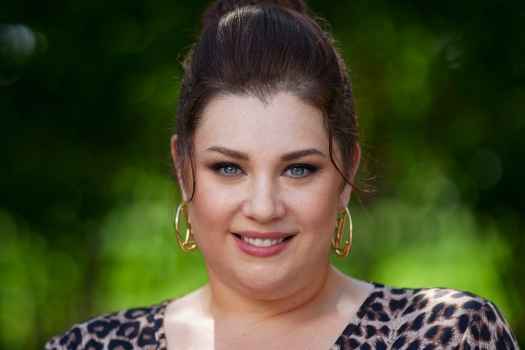 Participant Dina - person with auburn hair in an updo wearing a cheetah print shirt and smiling outside