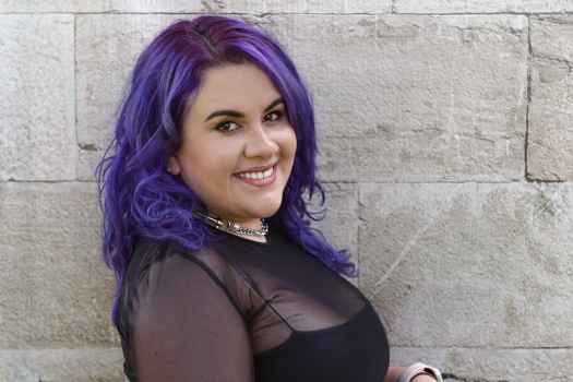 Participant Joanne - person with purple hair smiling in front of a grey stone wall