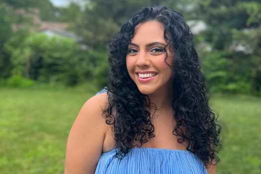 Participant Irene - person with long and wavy dark hair wearing blue and smiling outside