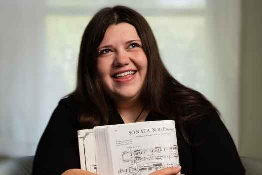 Participant Ashley - person with long dark hair smiling and holding sheet music