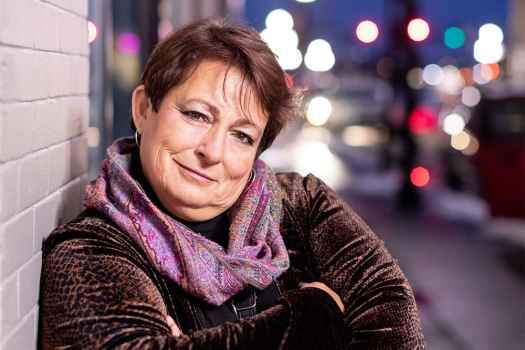 Woman wears lilac scarf and leans outside at dusk