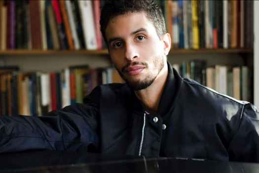 Participant Dylan is sitting behind a black grand piano wearing a black jacket