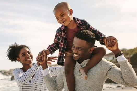 Family with kid on dad shoulders walk on beach