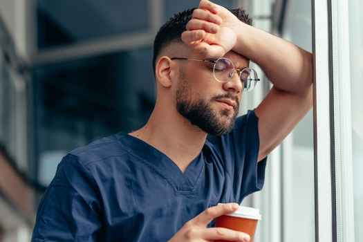 Nurse with coffee leans on window