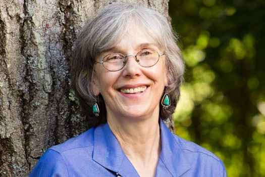 Participant Luanna - person with short grey hair smiling against a big tree trunk
