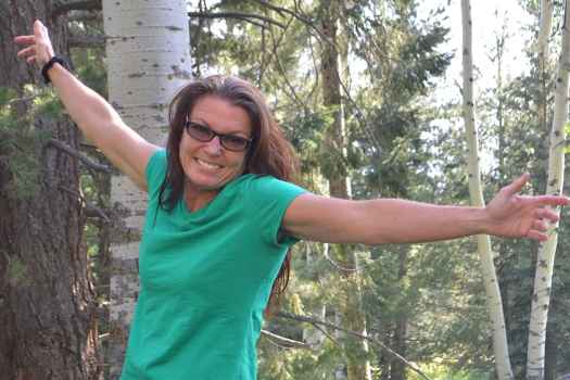 Deconstructing Stigma participant Debbie - person in green shirt and sunglasses arms flung out standing in woods
