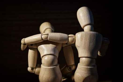 Artist mannequins posed on an embrace of support, black background