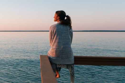Woman sits on railing, looking out to sea