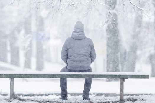 Figure sits on bench on snowy day