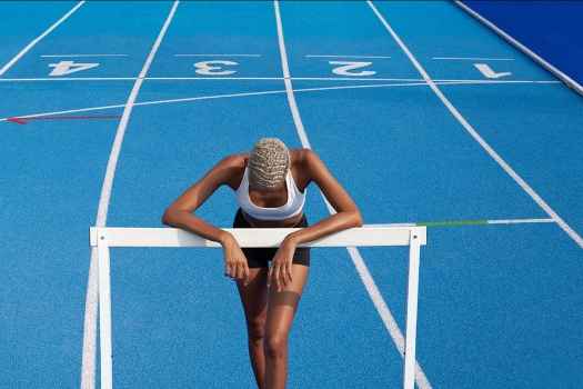 Athlete leans on hurdle on blue track