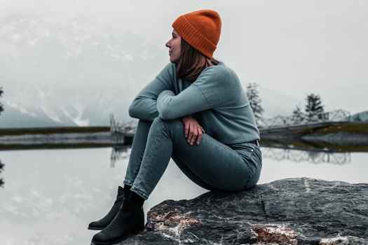Person sits on rock looking out at lake in gray winter