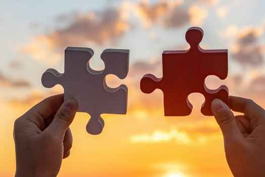 Two hands holding large jigsaw puzzle pieces in front of a sunset