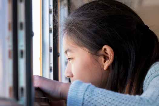Girl with long dark hair looking out an open school bus window