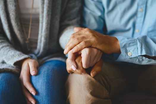 2 people sitting down and holding hands