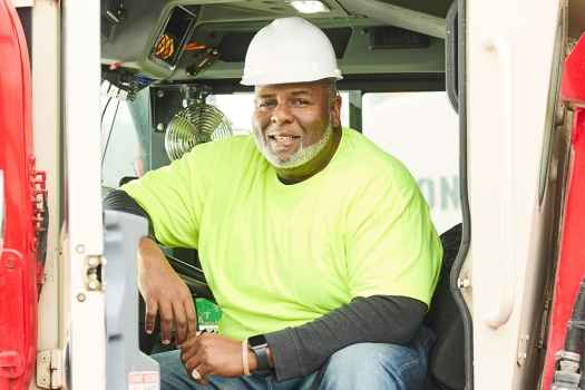 Deconstructing Stigma participant Julian - person in safety yellow shirt and hard hat in construction vehicle