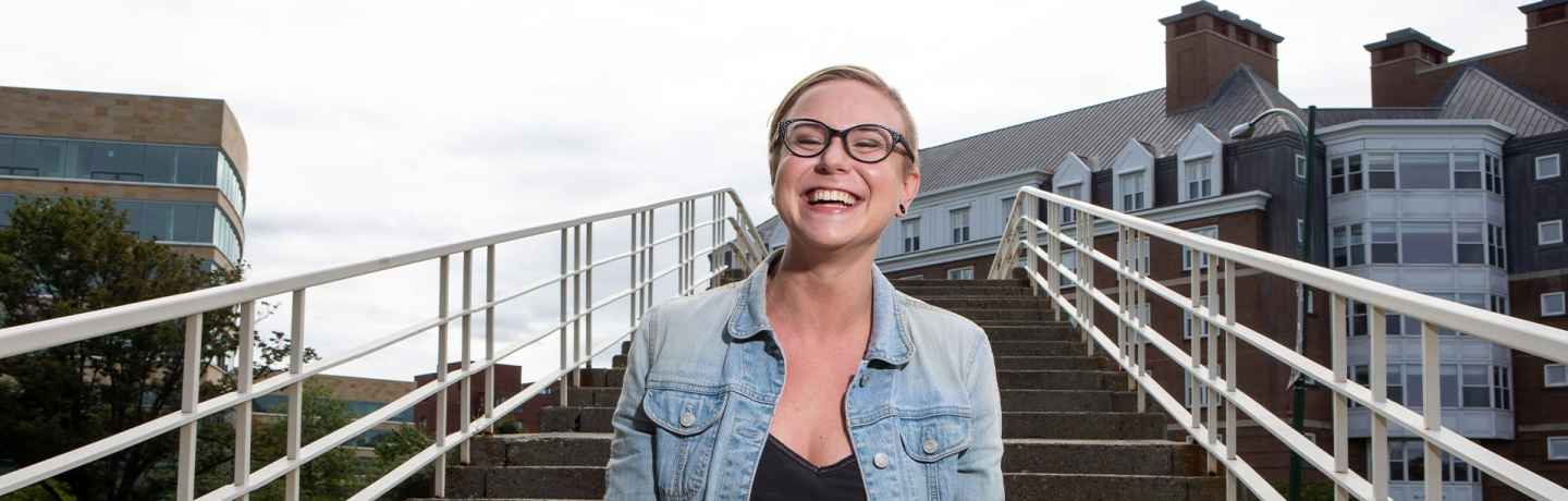 Participant Kelsey - person in glasses wearing a denim jacket and laughing, there is a staircase in the background