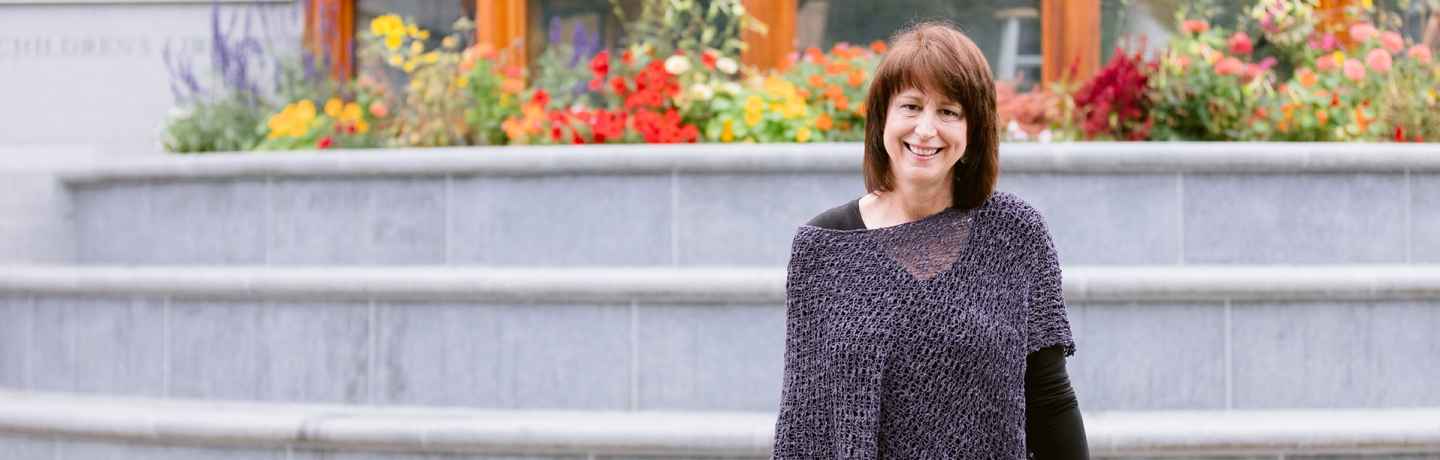 Participant Lise - person with dark hair wearing a purple sweater smiling on grey stairs