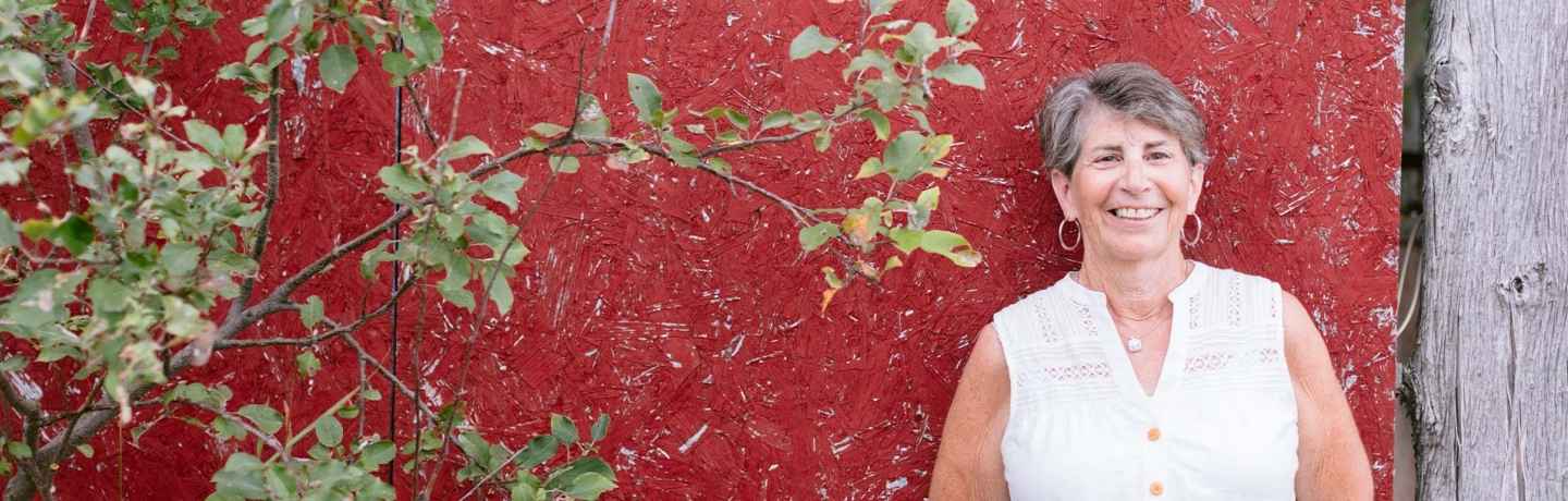 Participant Linda - person with short hair and a white tank top smiling in front of a red wall