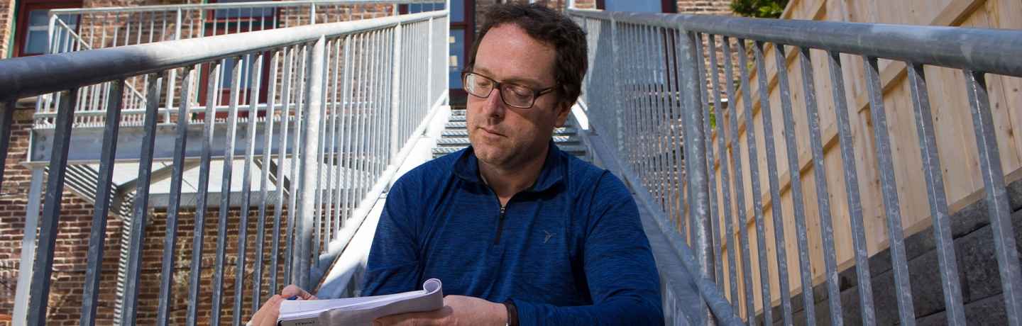 Participant Thomas - person with short brown hair sitting on an outdoor staircase looking at papers