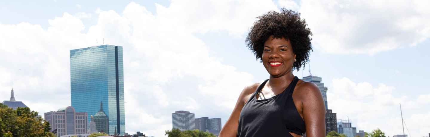 Participant Nieisha - person with dark curly hair smiling in front of the Boston skyline