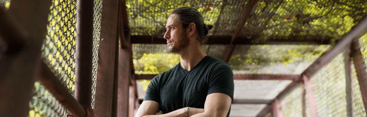 Deconstructing Stigma participant Sean - person stands in chainlink fence bridge