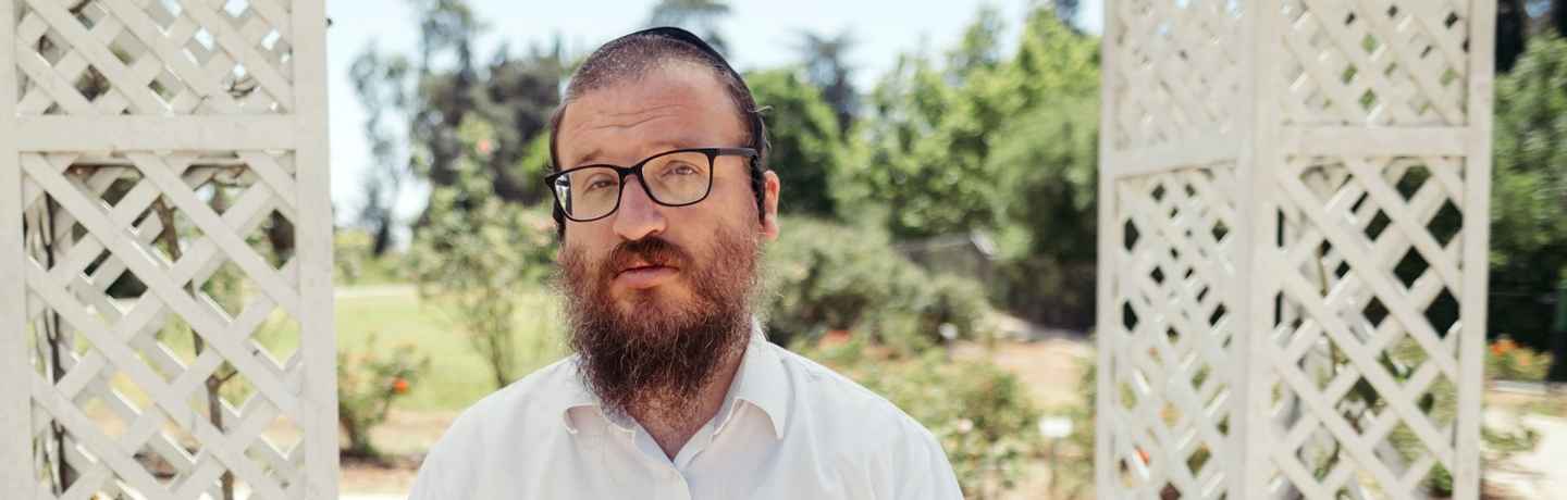 Deconstructing Stigma participant Yakov - Person in white shirt stands outside by box trellis