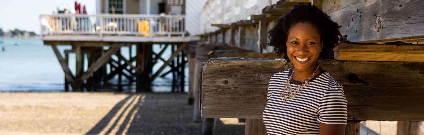 Participant Ivy - person with short curly hair leaning against a wooden structure