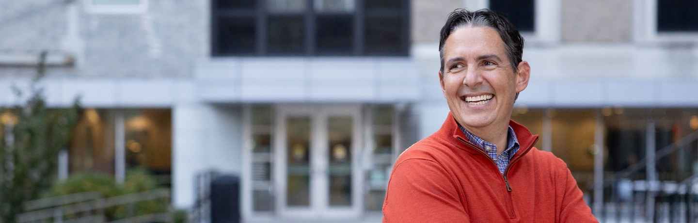 Participant Jeremy - person with short dark hair in a red sweater smiling outside a building