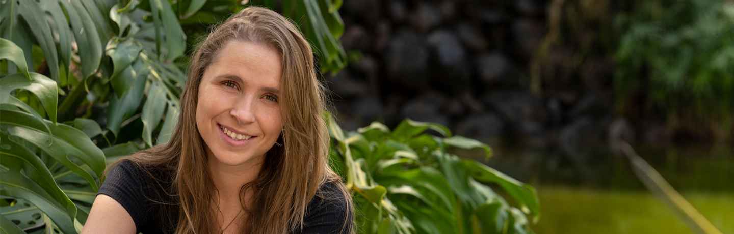 Deconstructing Stigma participant Andrea - person sits by river with big tropical leaves in background