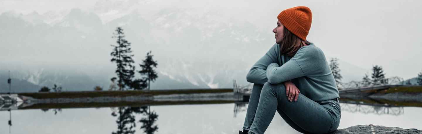 Person sits on rock looking out at lake in gray winter