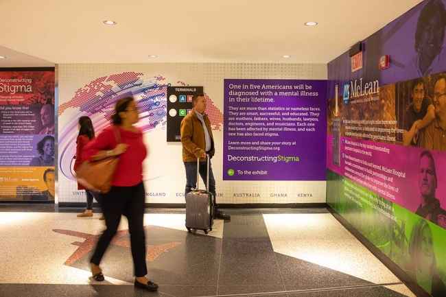 Multiple people with suitcases walking past and looking at a Deconstructing Stigma display