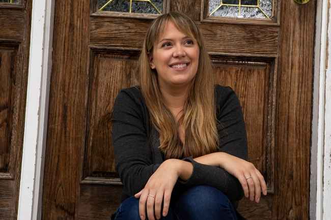 Participant Kimberly - person in sweater smiling in front of a wooden door