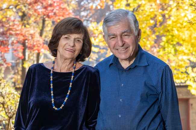 Participant Kitty - person with brown hair in front of colorful fall foliage smiling next to a person in a blue button-down shirt