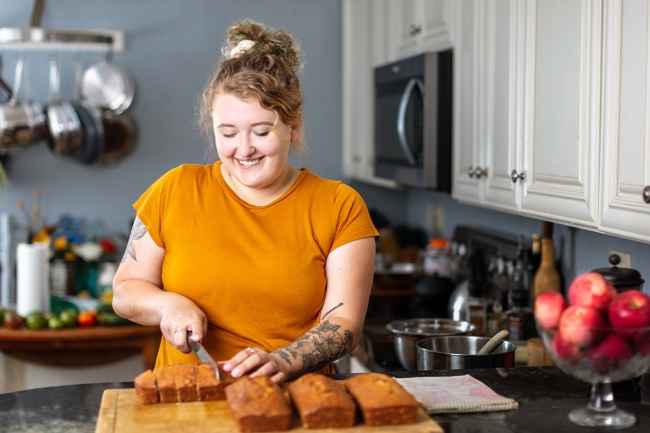 Participant Lexi - person with curly hair in an orange shirt cutting pastries in a kitchen