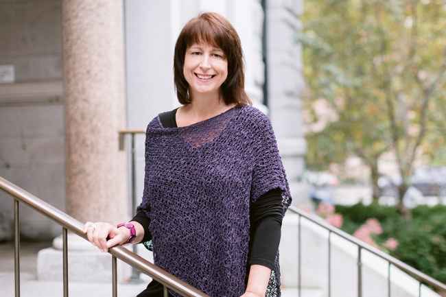 Participant Lise - person with dark hair wearing a purple sweater smiling on grey stairs
