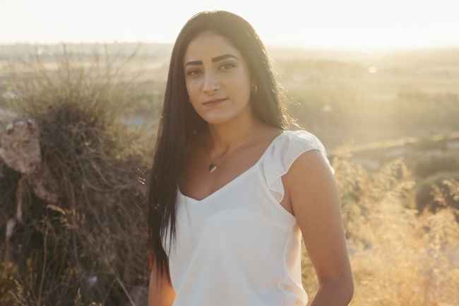 Deconstructing Stigma participant Rotem - person with long dark hair and white shirt standing in field 